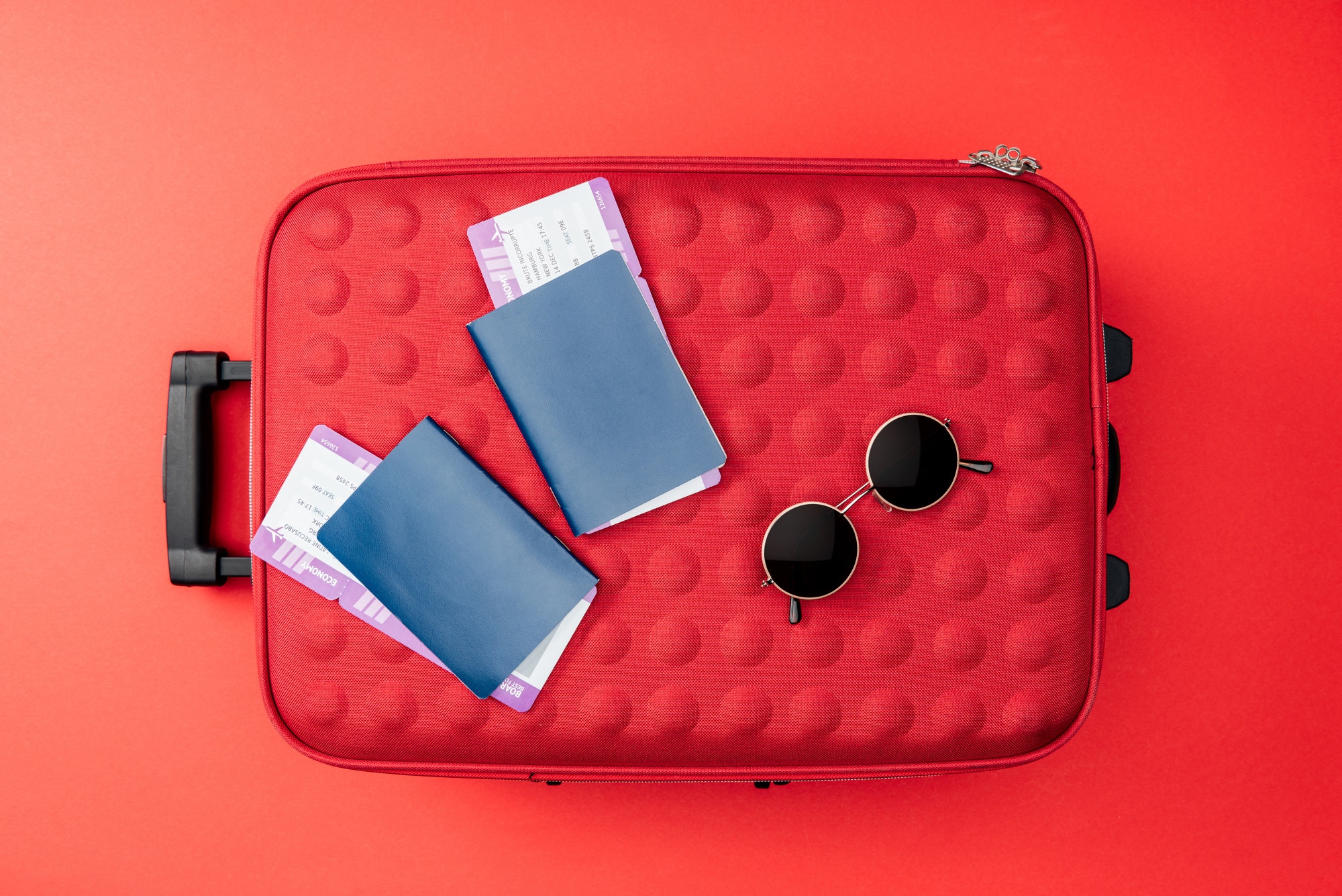 top-view-of-travel-bag-passports-air-tickets-and-sunglasses-on-red-background